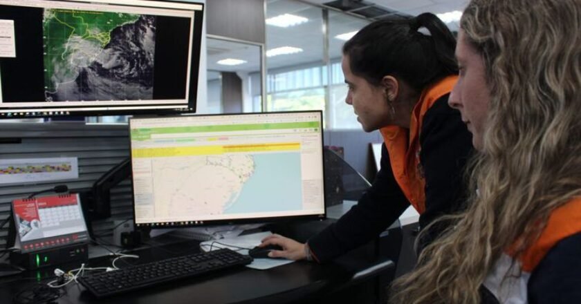 Duas mulheres meteorologistas observam tela de computador com radar meteorológicos.