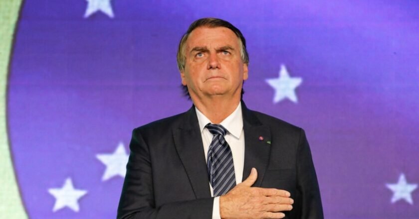 Jair Bolsonaro diante de uma bandeira do Brasil, no telão, com a mão direita sobre o peito.