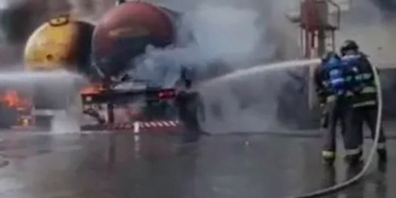 Bombeiros lançam água sobre caminhões. É possível ver chamas na parte de baixo dos caminhões e muita fumaça.