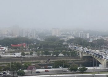 Céu coberto por nuvens. Nevoeiro sobre os prédios da zona norte de São Paulo. Na parte de baixo da foto, a Marginal TietÊ com vários carros passando.