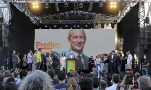 Ciro Gomes no centro da foto que mostra dezenas de pessoas no palco, ao seu lado, e no público, enquanto ele faz discurso. Ao fundo, uma foto grande de Ciro.
