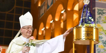Dom Cláudio Hummes estende a mão na direção da imagem de Nossa Senhora aparecida. Enquanto segura uma rosa com a outra mão.