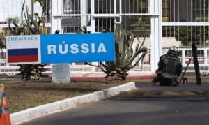 Militar aparece abaixado perto do portão da embaixada da Rússsia. Ao lado dele, uma placa traz a bandeira da Rússia e o nome do país.