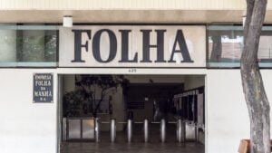 Fachada do prédio da Folha de São Paulo, na Capital. Mostra catracas de controle de acesso na entrada e uma placa escrito "Folha" no alto da porta de entrada.
