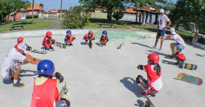 Crianças em círculo, usando equipamentos de segurança, fazem alongamento antes da aula de skate.