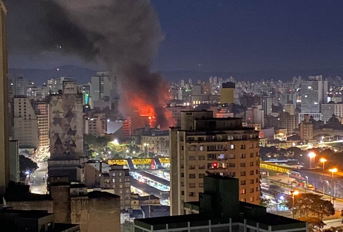 Fumaça e claridade provocada pelas chamas aparecem no meio de prédios em uma foto panorâmica.