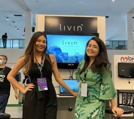 Synde Libório  e Luana Rosas, da Livin, aparecem diante de um totem da empresa durante evento.