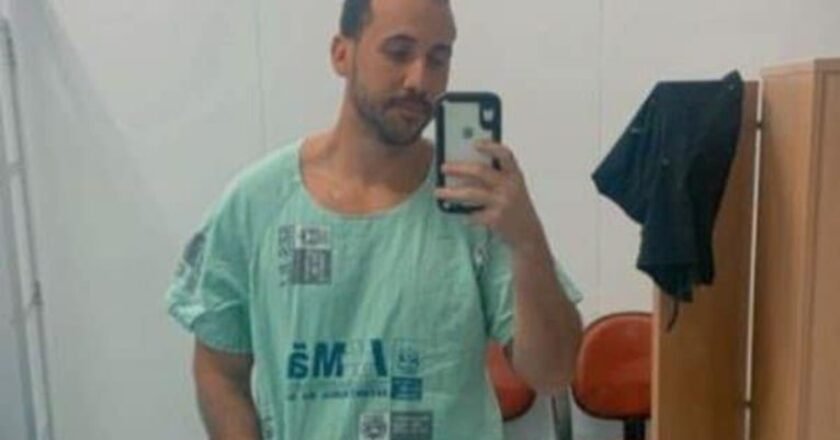 Médico, usando roupa hospitalar, faz selfie diante de um espelho.