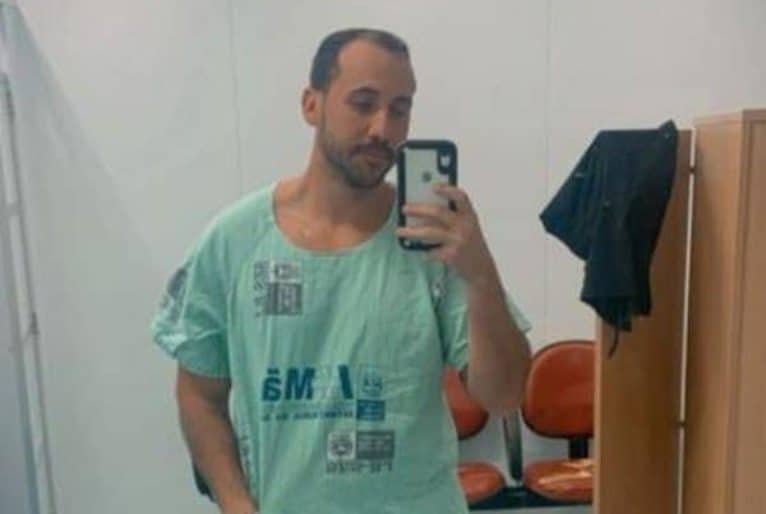 Médico, usando roupa hospitalar, faz selfie diante de um espelho. 