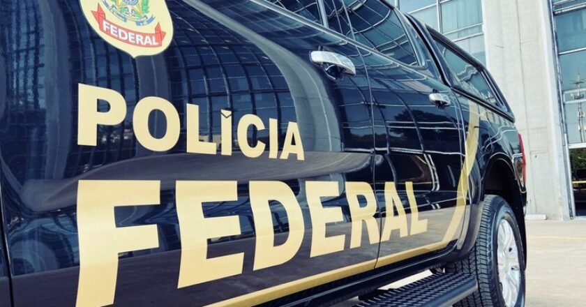 Viatura da Polícia federal parada em frente a prédio espelhado. Na lataria é possível ver escrito Polícia Federal e o logo da corporação.