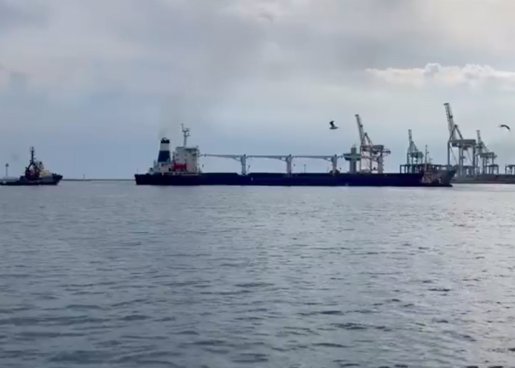 Navio carregado deixa o porto da Ucrânia. Foto tirada a distância mostra o mar e um pequeno barco perto do navio.